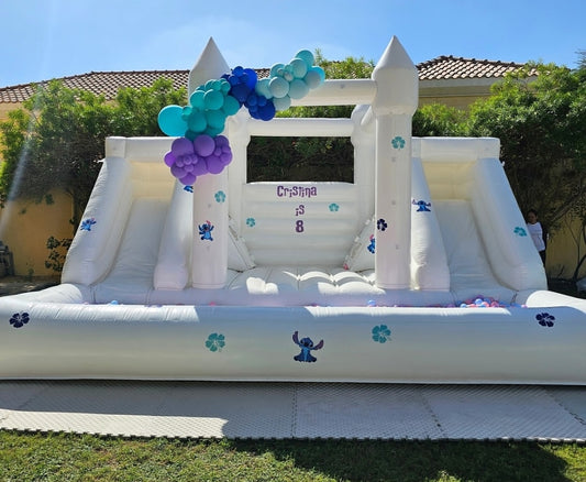 White double slide bouncy castle with ballpit from Aura Luxury Rental Ltd, featuring colorful slides and a spacious play area.