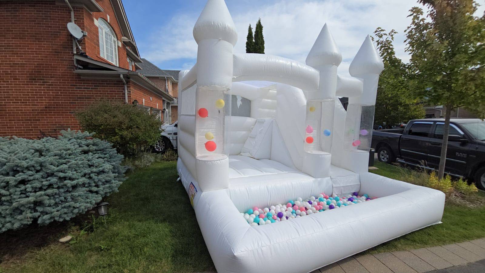 White balloon pillar castle with slide and ballpit for kids, designed by Aura Luxury Rental Ltd, featuring colorful play elements.