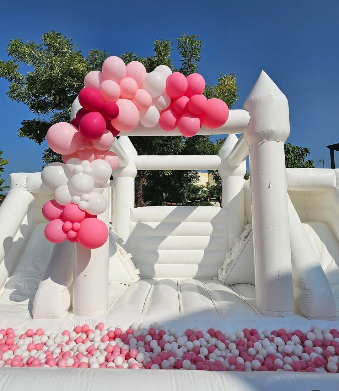 White double slide bouncy castle with ballpit from Aura Luxury Rental Ltd, featuring colorful slides and a spacious bouncing area.