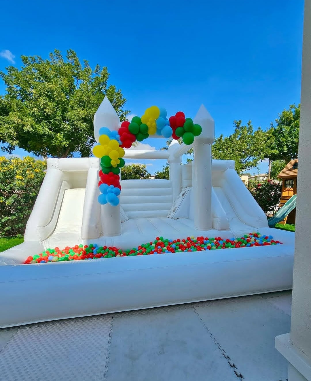 White double slide bouncy castle with ballpit by Aura Luxury Rental Ltd, featuring colorful slides and soft inflatable surfaces.
