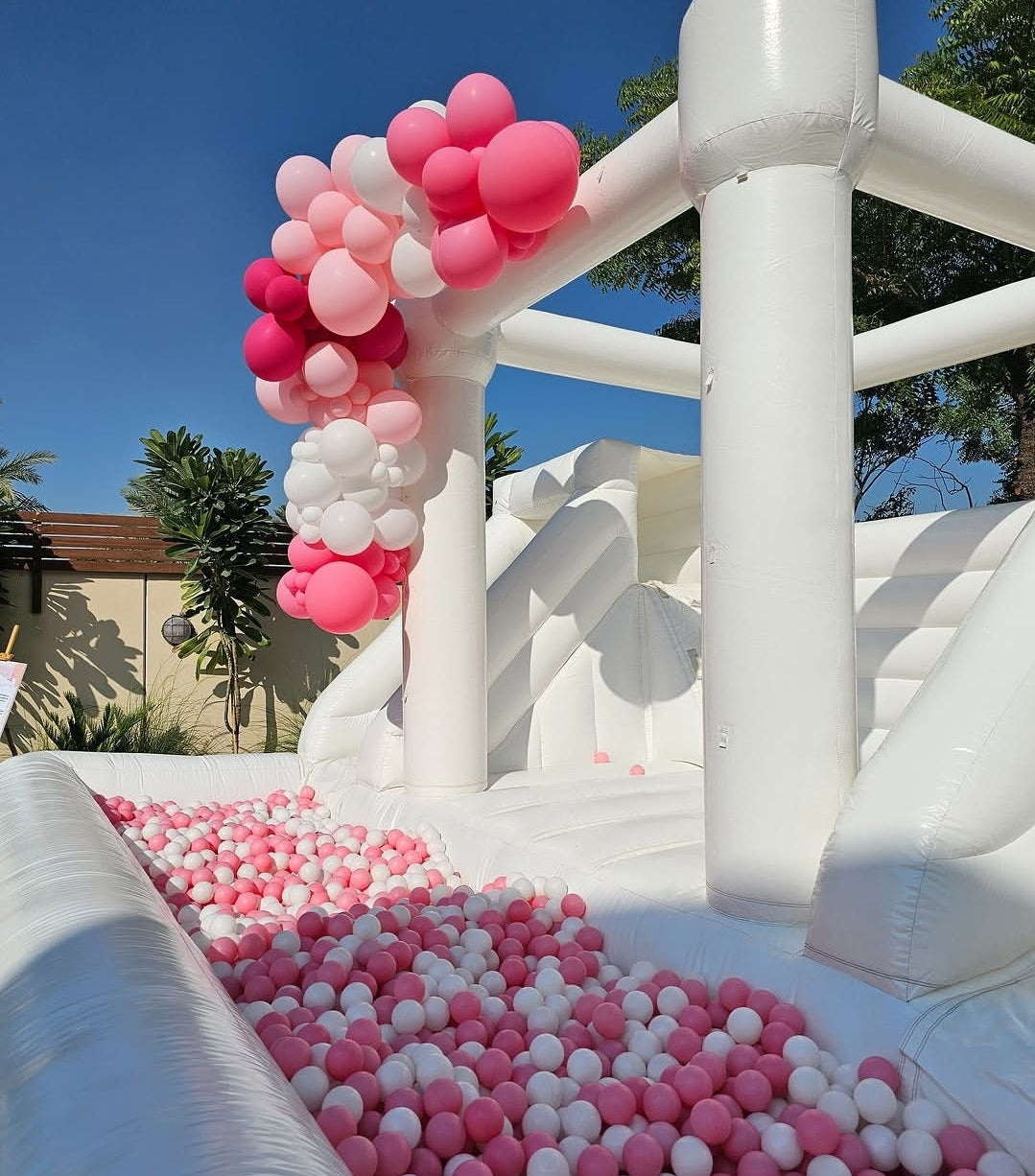 White double slide bouncy castle with ballpit from Aura Luxury Rental Ltd, featuring colorful slides and a spacious play area.