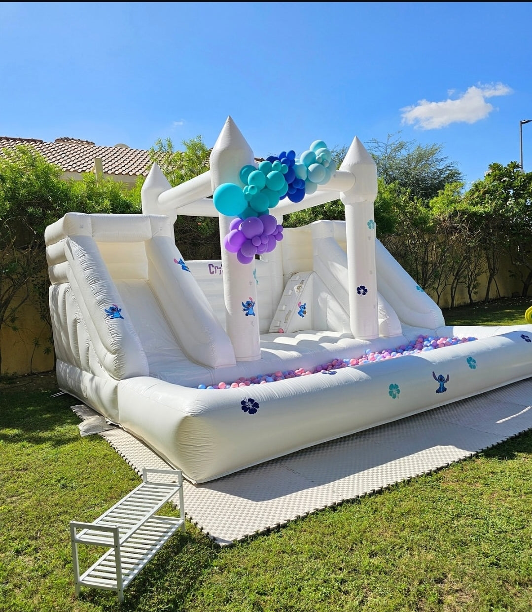 White double slide bouncy castle with ballpit from Aura Luxury Rental Ltd, featuring colorful slides and soft bounce areas.